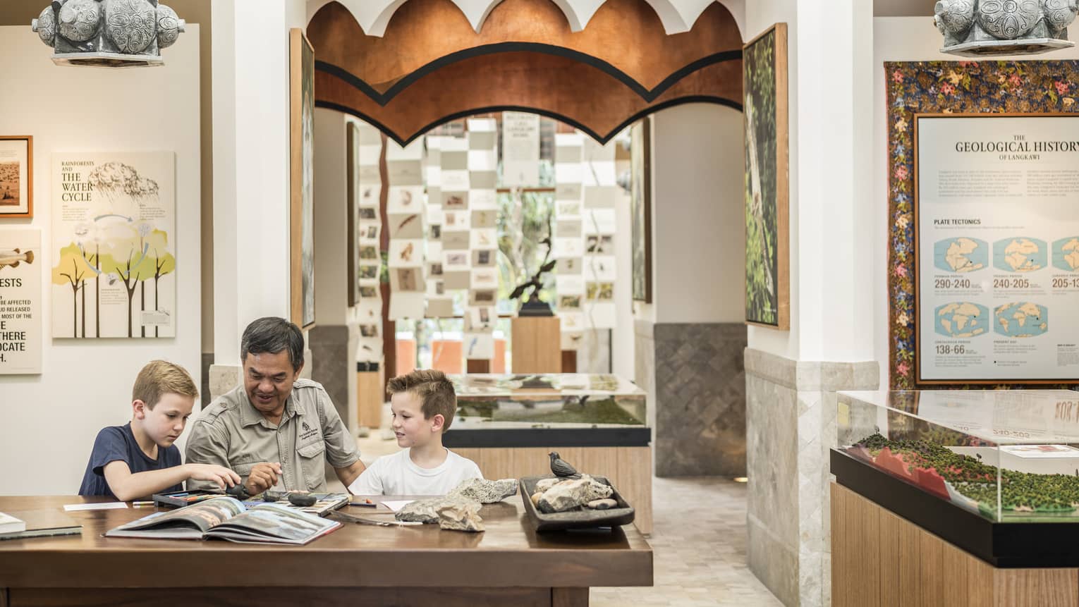 A man and two kids reading a book together at the Mangroves Discovery Centre at Four Seasons Langkawi