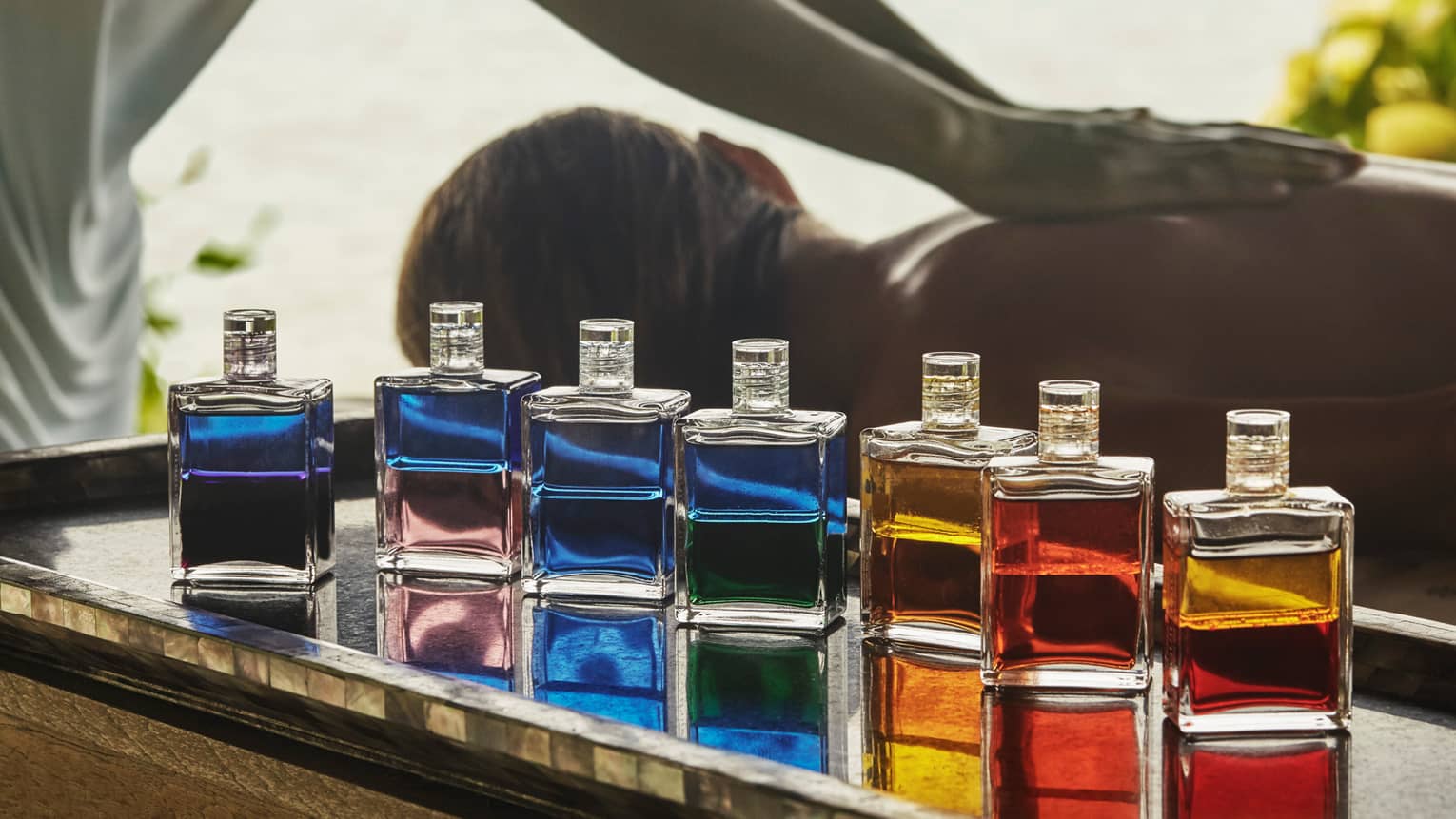 Spa staff massages woman's back behind row of colourful glass bottles with oils