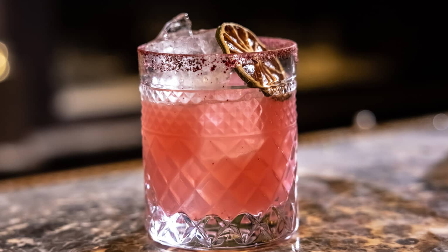 A pale pink cocktail garnished with dried citrus slice