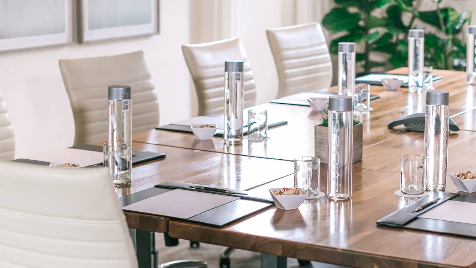A rectangular boardroom table set with clear glass water bottles and black folders in a naturally-lit room