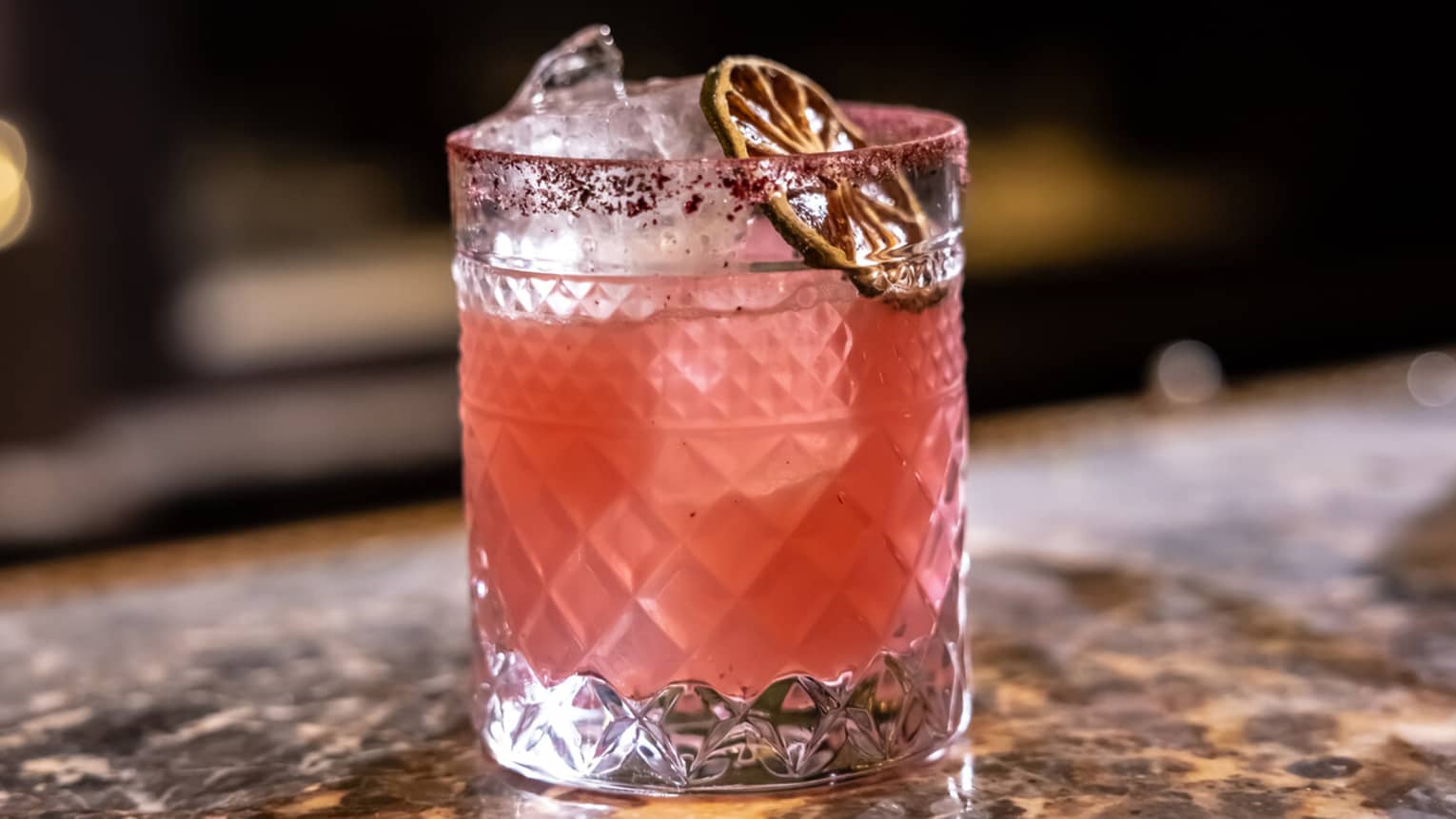 A pale pink cocktail garnished with dried citrus slice