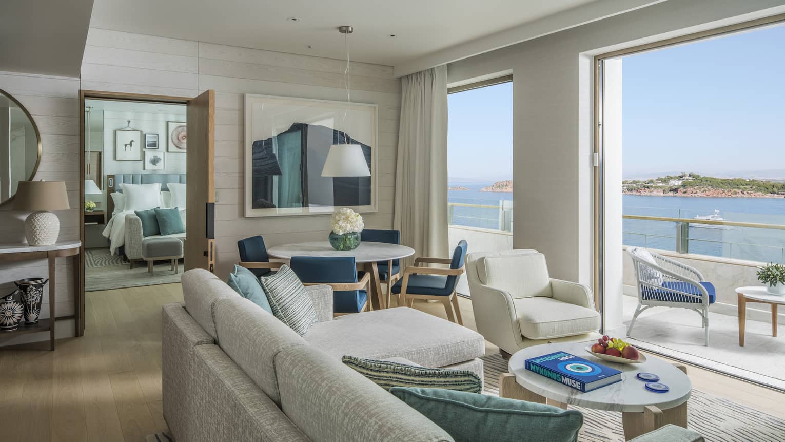 Light-filled living room with off-white sofa and arm chair, plus dining area, looking out to sea