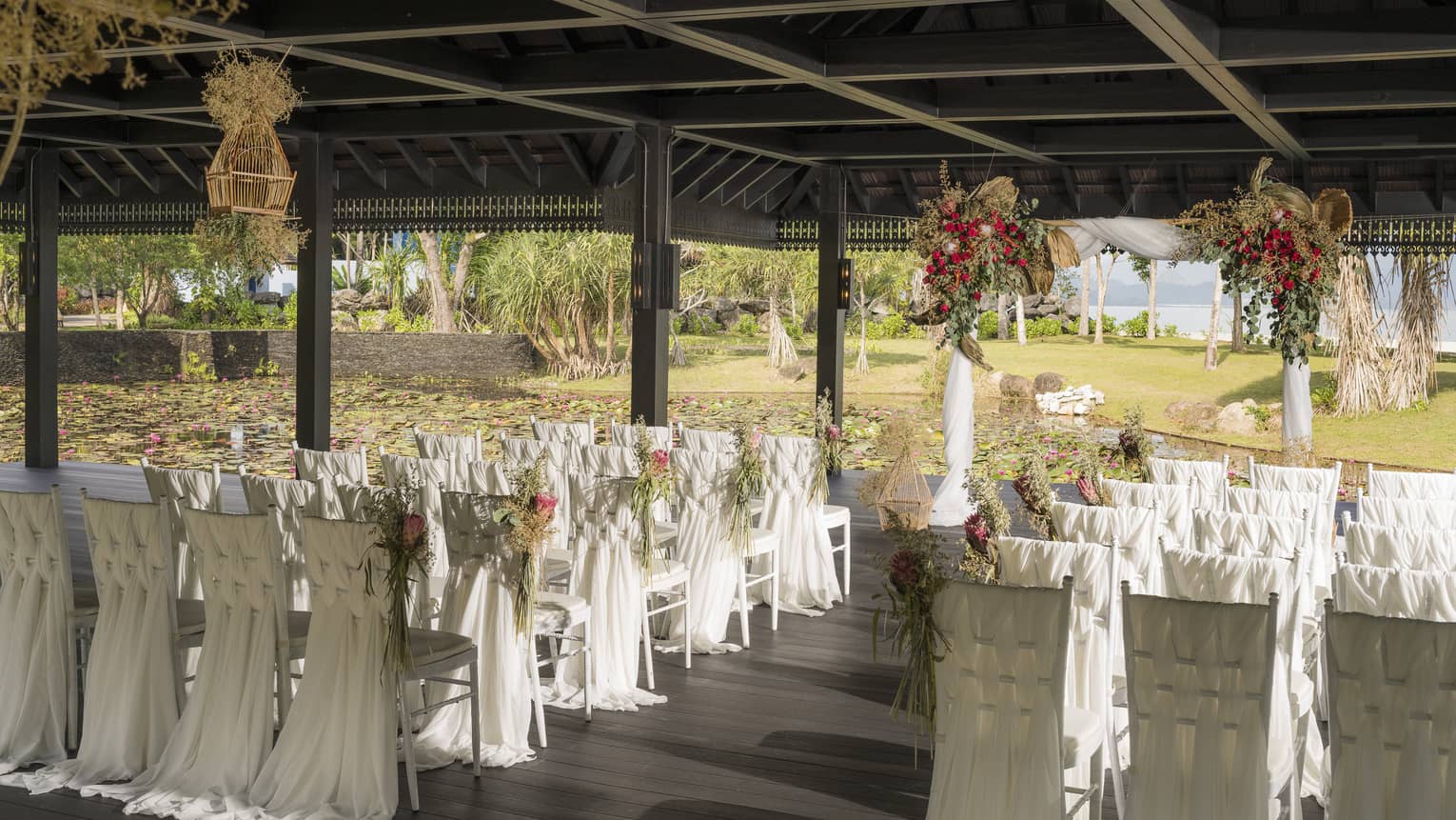 Outdoor wedding reception under pavilion, rows of chairs with white linens 