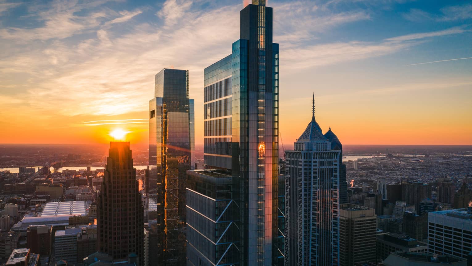 Philadelphia’s skyscrapers soaring above an expansive city, with a sunset-illuminated sky in the background.
