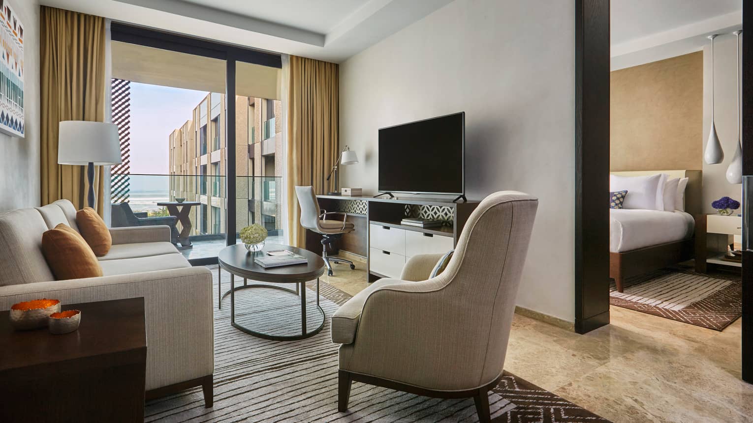 Four Seasons Deluxe Suite modern beige sofa, armchair, TV, large glass door to balcony
