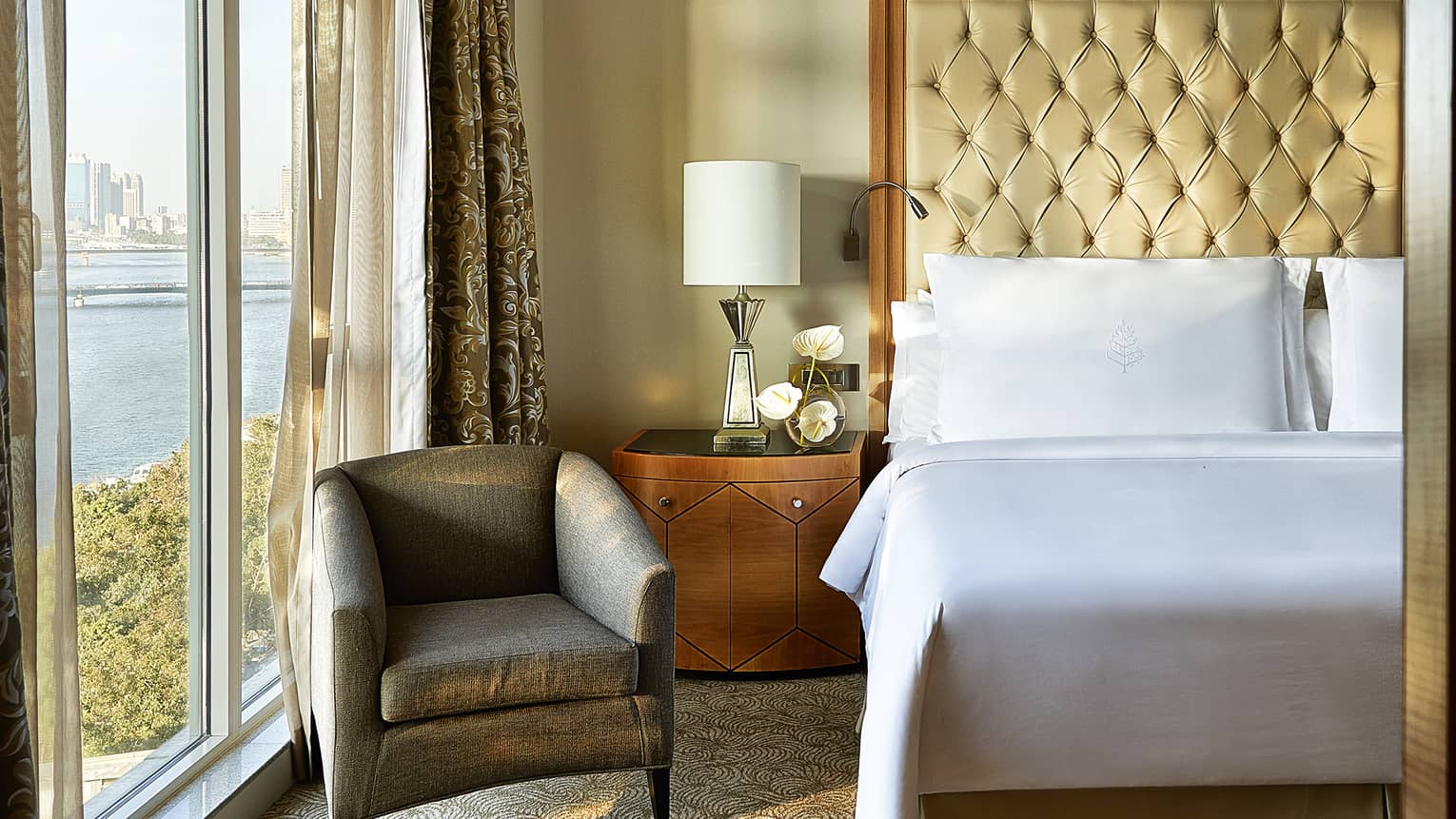 Royal Suite close-up of white pillows and tall leather headboard, wooden side table with lamp and white orchids