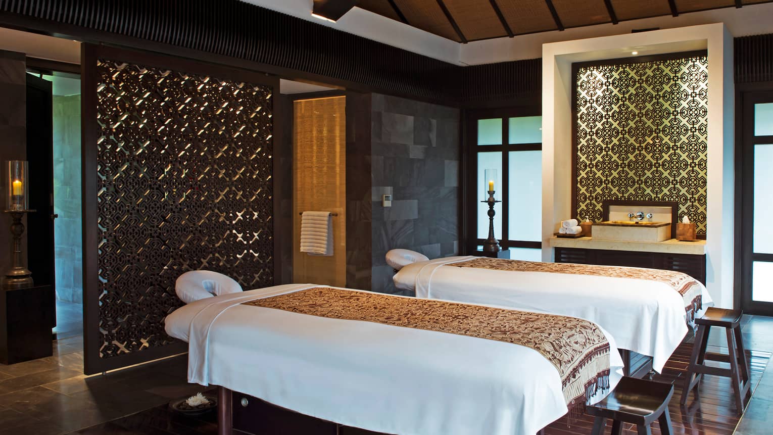Couples massage tables side-by-side in spa treatment suite with decorative walls