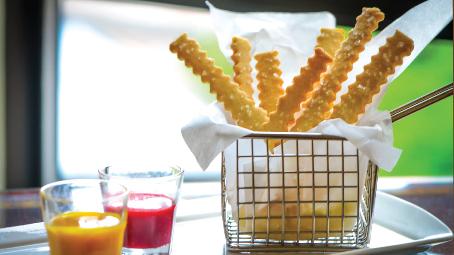Basket of crinkly French fries on a silver tray with ketchup and mustard dipping cups