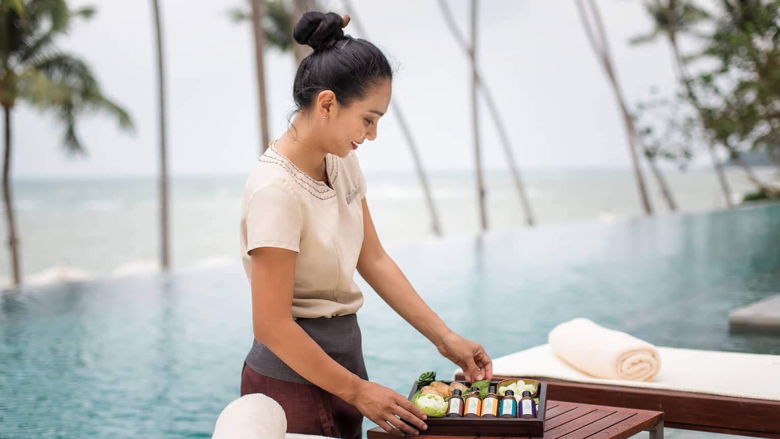 Spa attendant stands in front of swimming pool, holds wood box with bottles, soaps