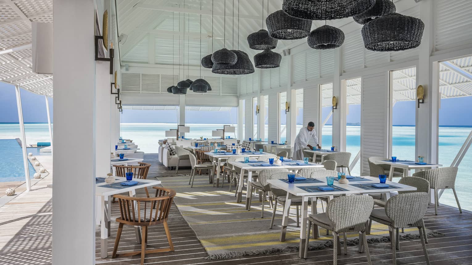 Wicker lanterns hang above clean place-settings adjacent to the ocean at the Blu Beach Club