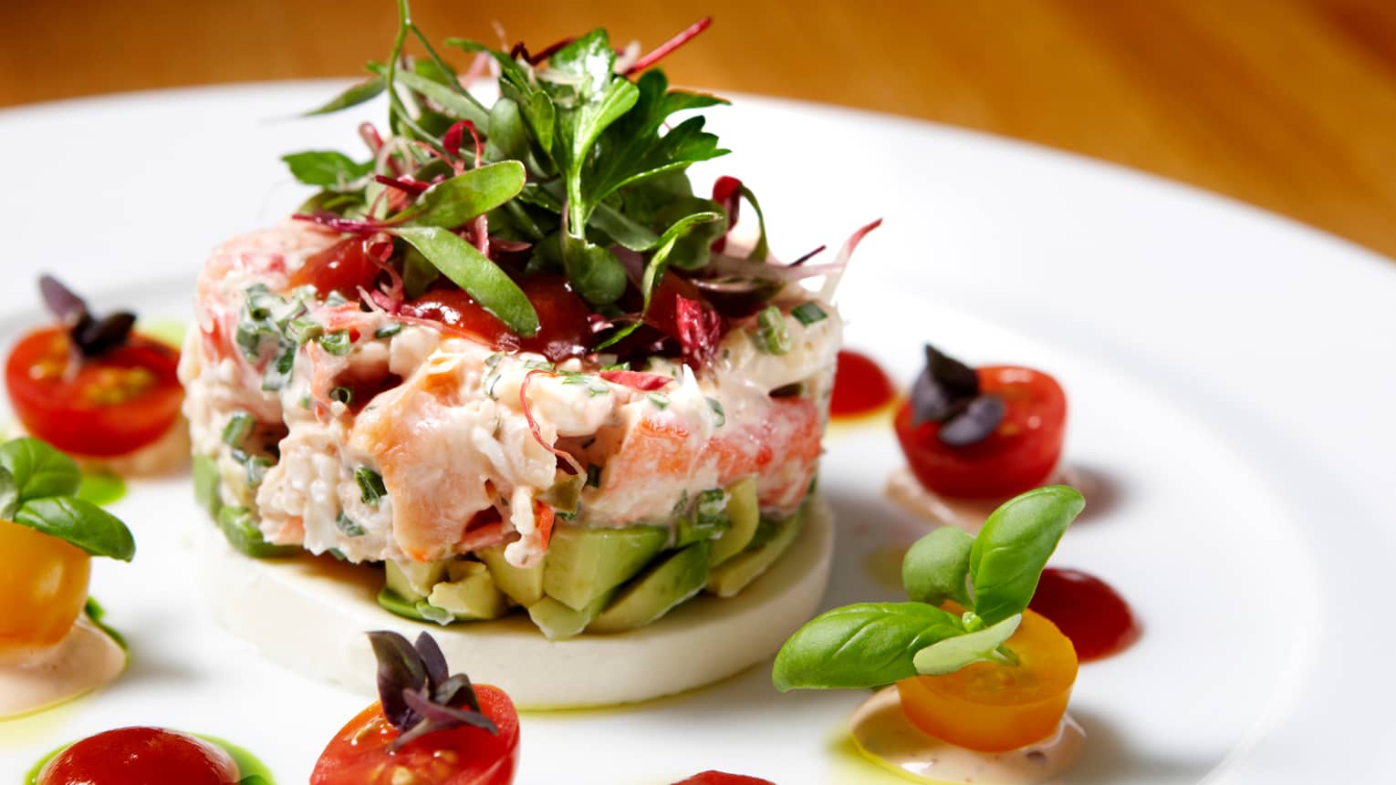Round Dungeness Crab with chopped avocado, greens garnished with tomatoes, basil