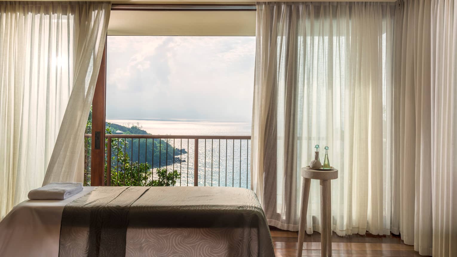 Massage bed in front of open window with long white curtains, ocean view 