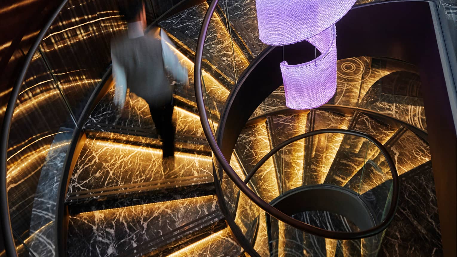 Server in uniform walks up black marble spiral staircase with orange lights 