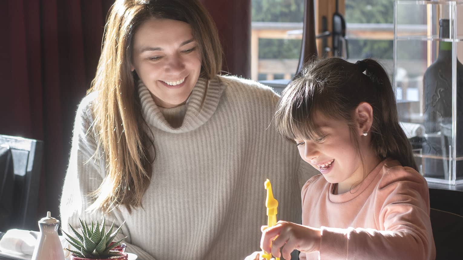 Mom and daughter smiling as daughter picks up sushi from bento box with chopsticks