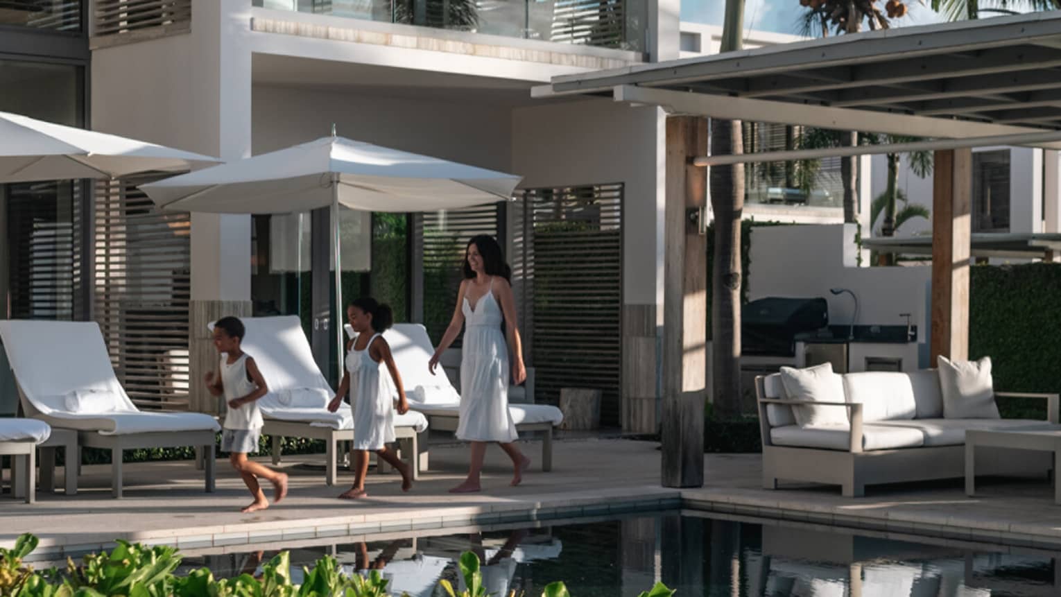 A woman and two children walking by a pool in an outdoor patio area of a villa 