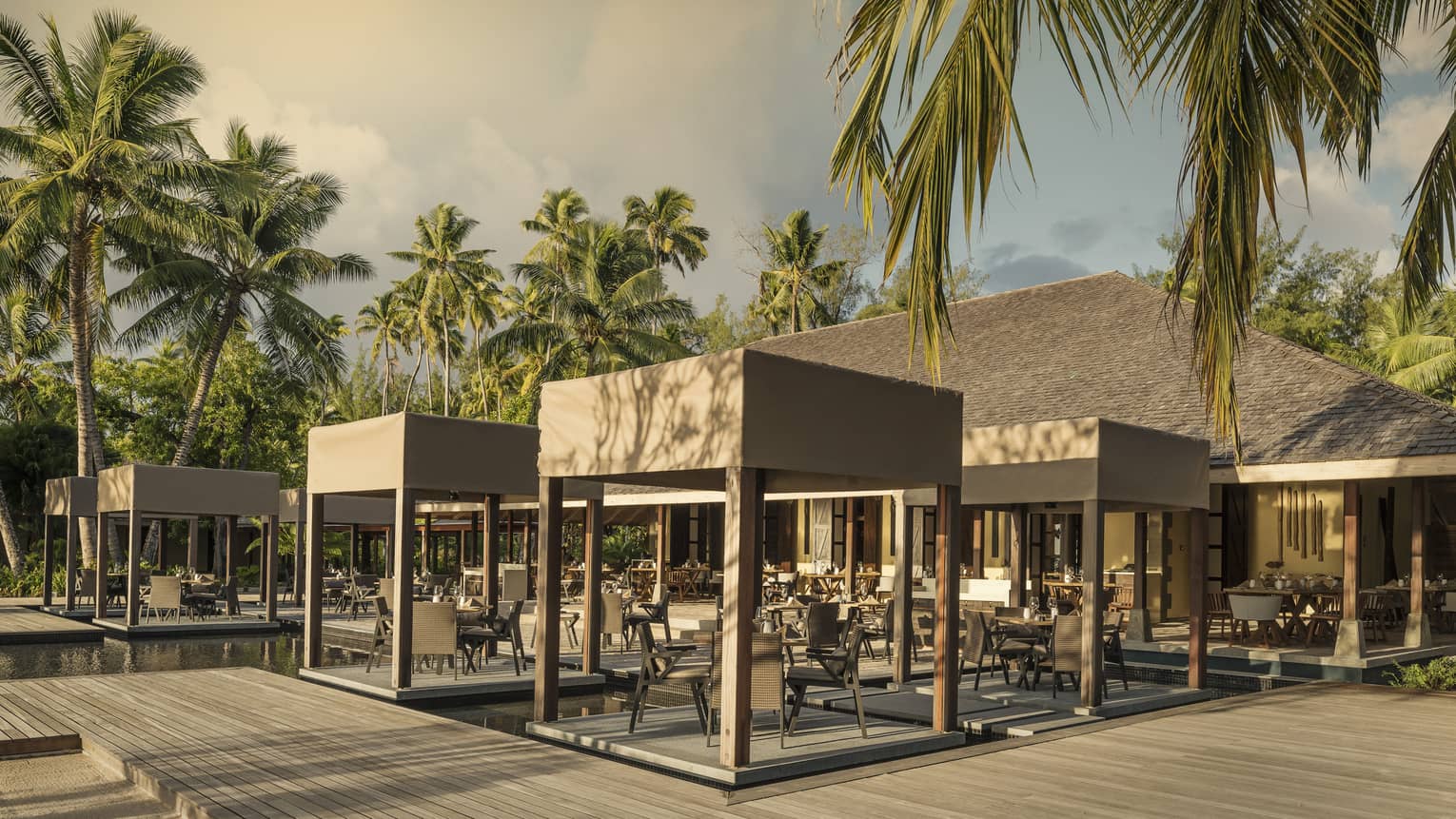 Outdoor Claudine restaurant with tables on decks over water, covered with wooden canopy 