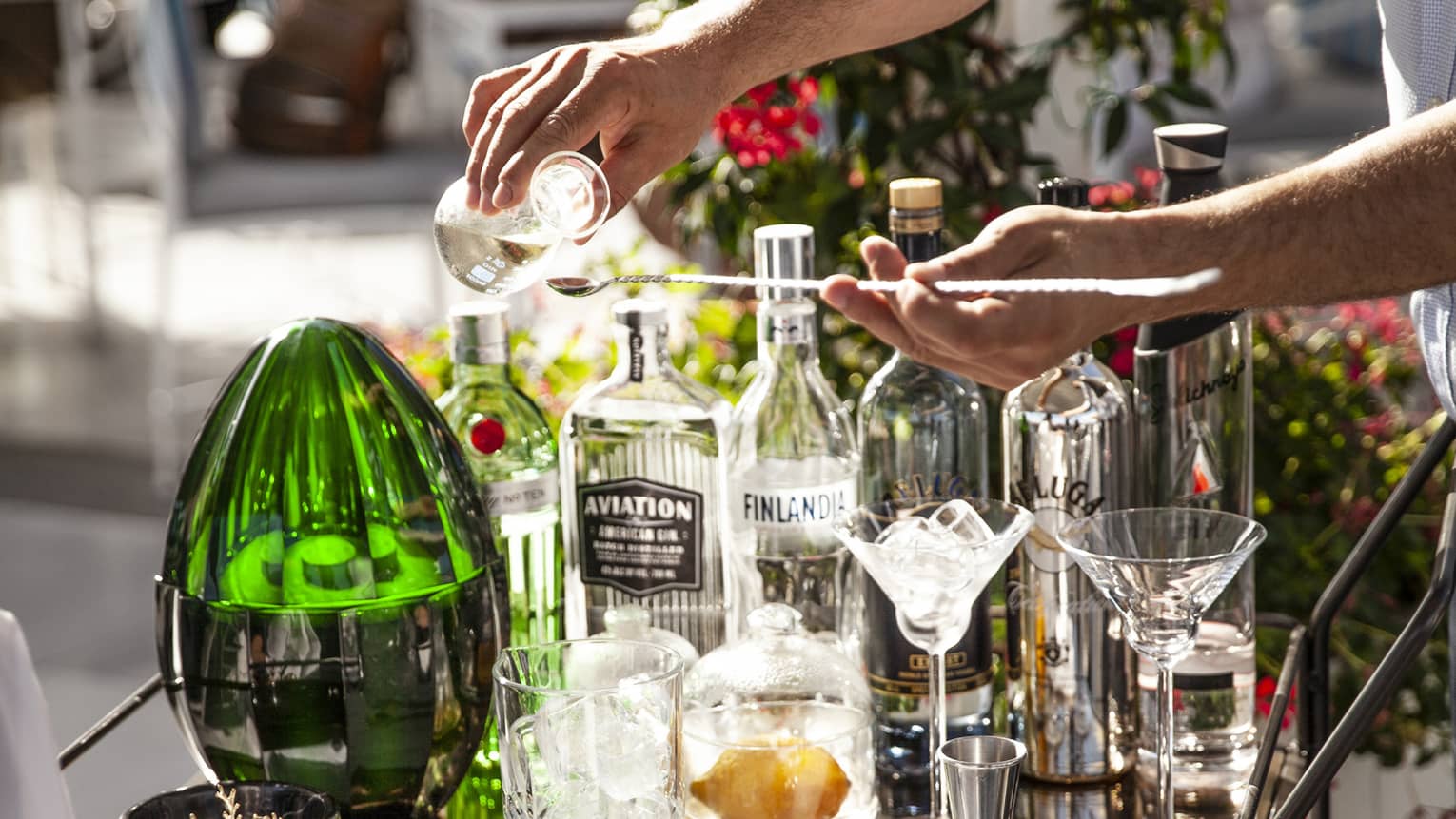 Man pours a drink at outdoor cocktail service cart with various glass bottles