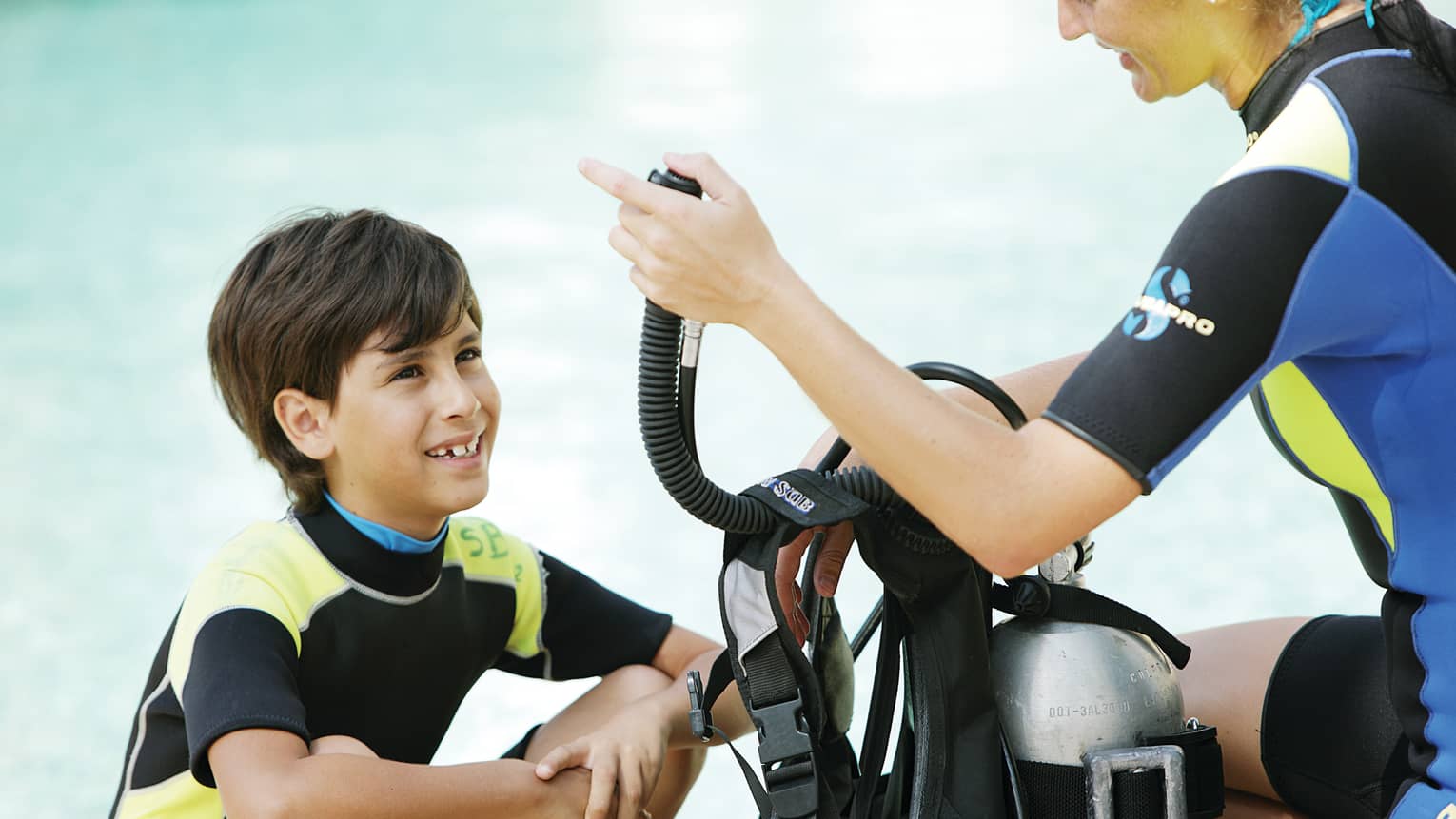 Boy in wetsuit in front of woman giving scuba diving instruction