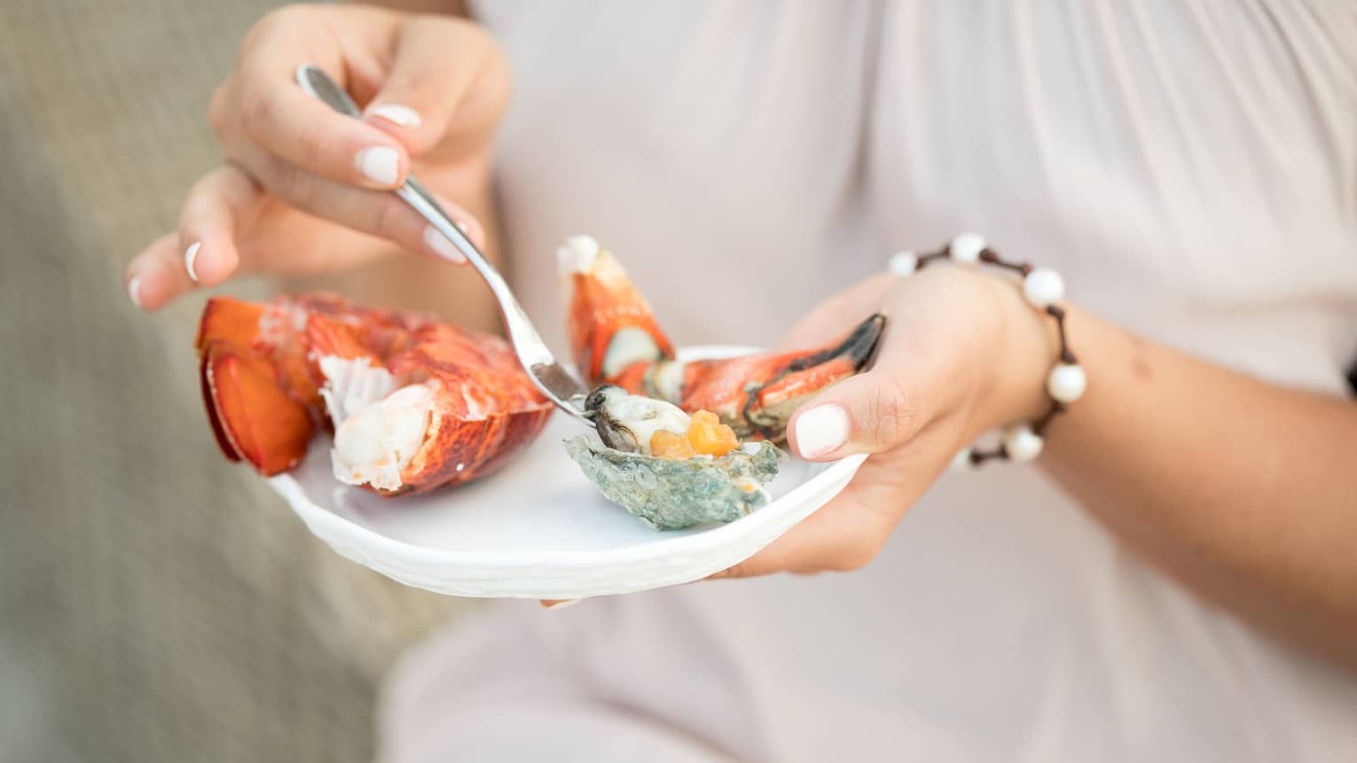 Close-up of woman holding small plate with fresh seafood, digging fork into oyster