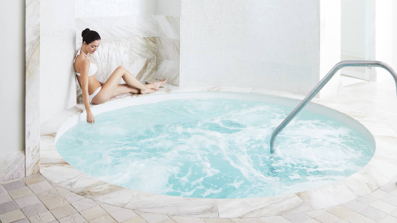 A woman relaxes by a marble hot tub in the spa