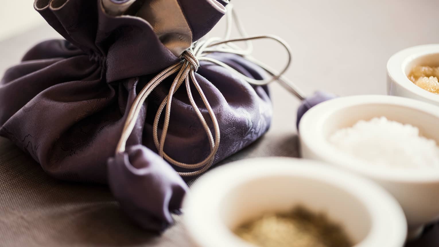 Dark silk pouch with tie behind small white ceramic bowls with spa salts