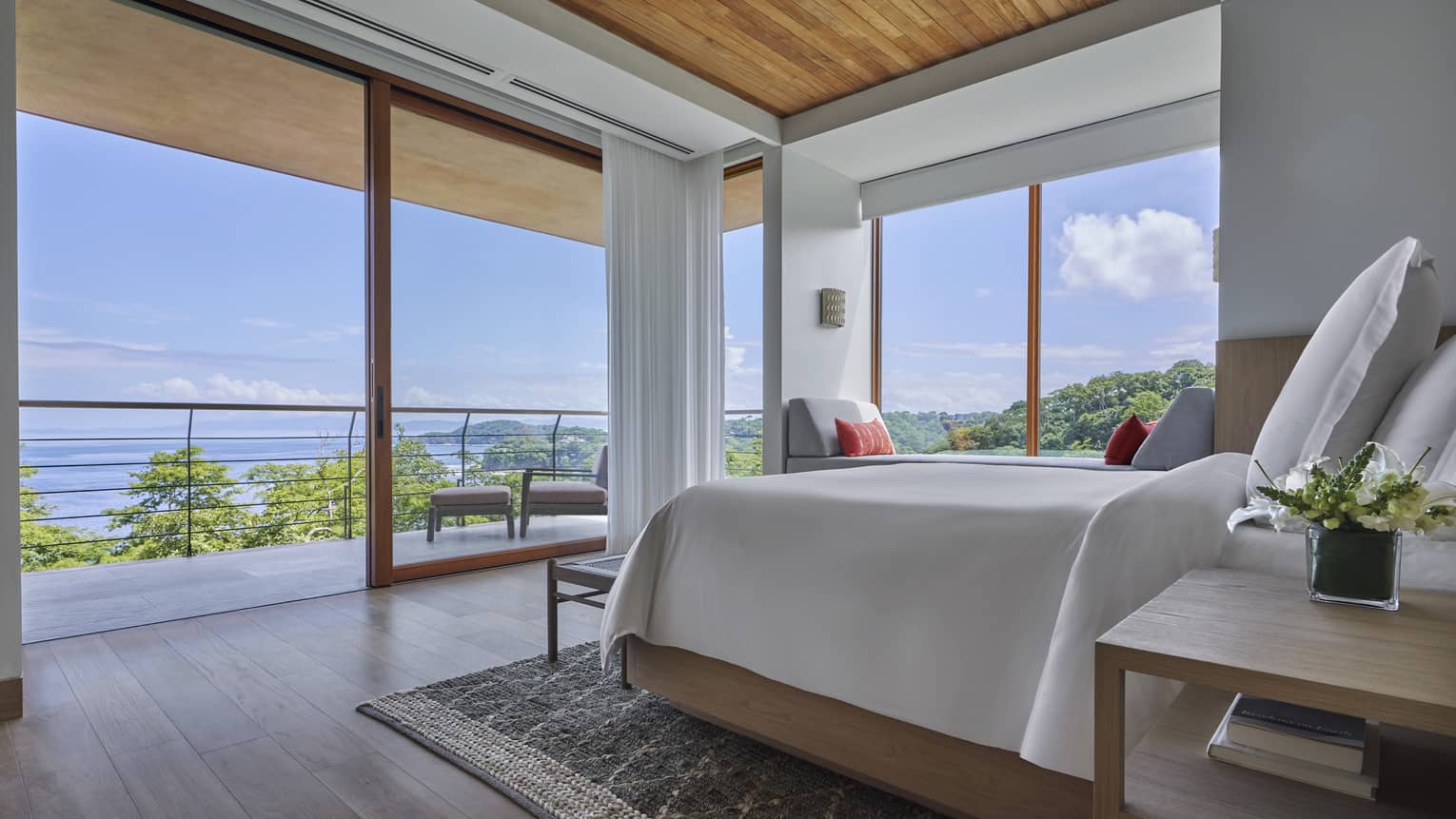 Bedroom with white king bed, two walls of windows looking out to the sea