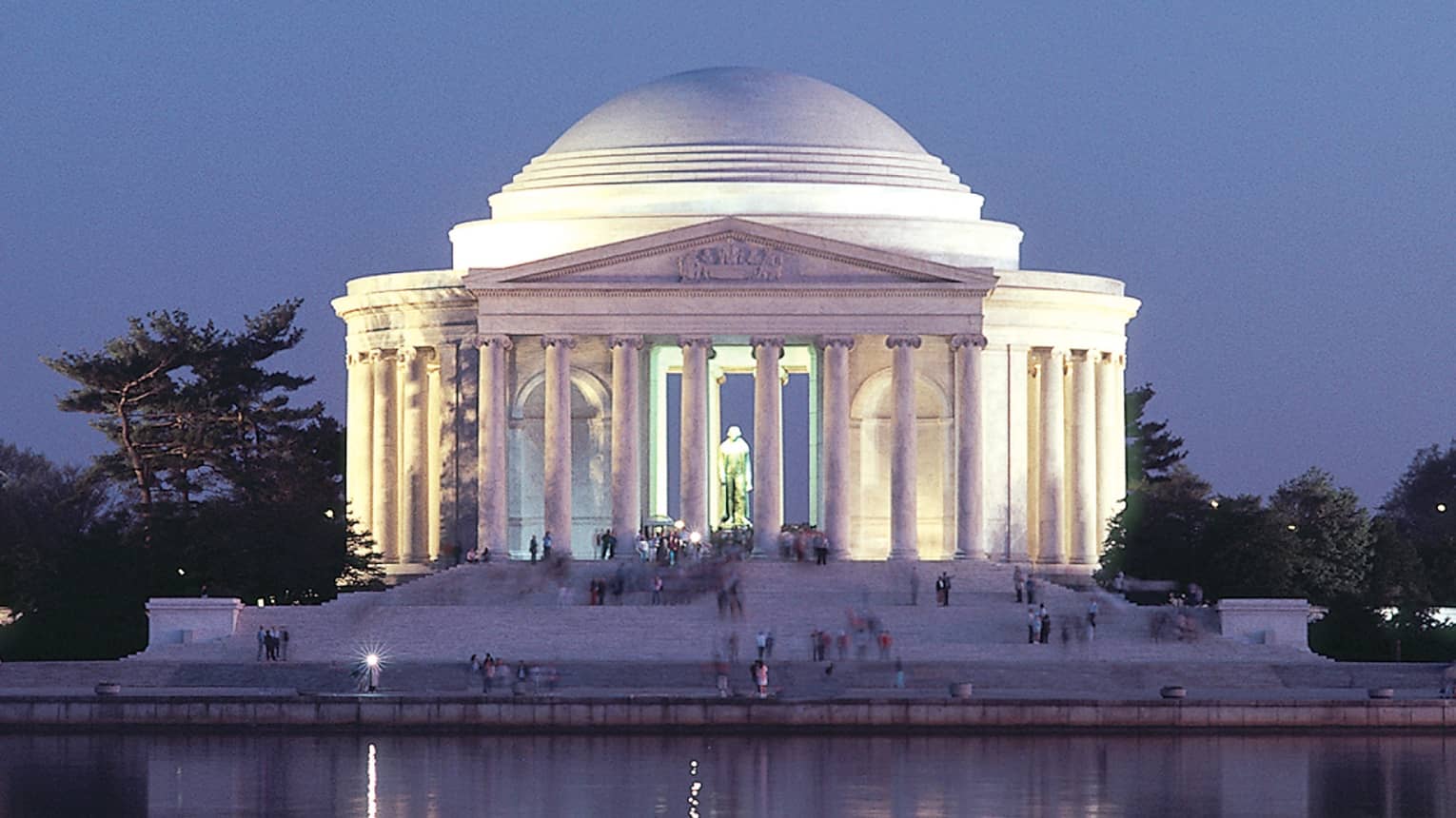 A large historical monument of white pillars and a large dome next to water.