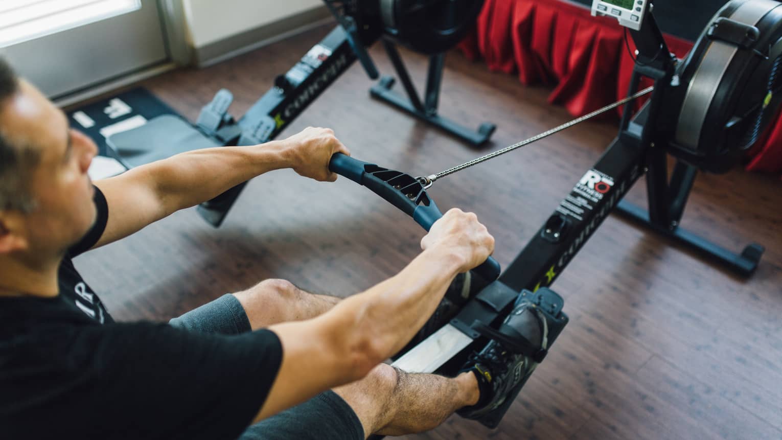 Man sits, pulls handle of cardio rowing machine in fitness facility