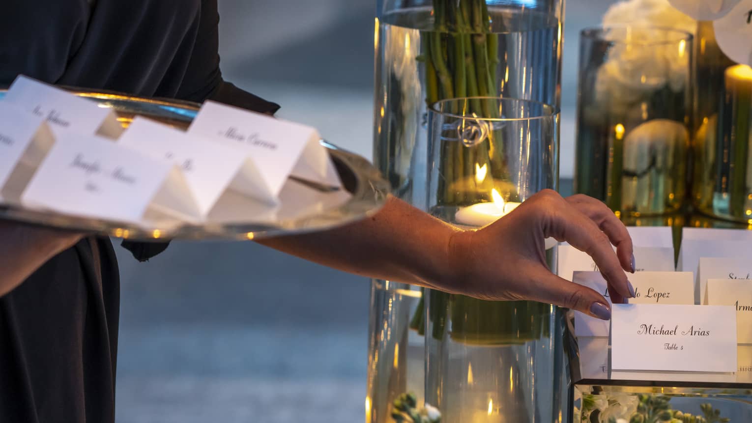 Close-up of hands placing name cards on banquet table with candles, flowers