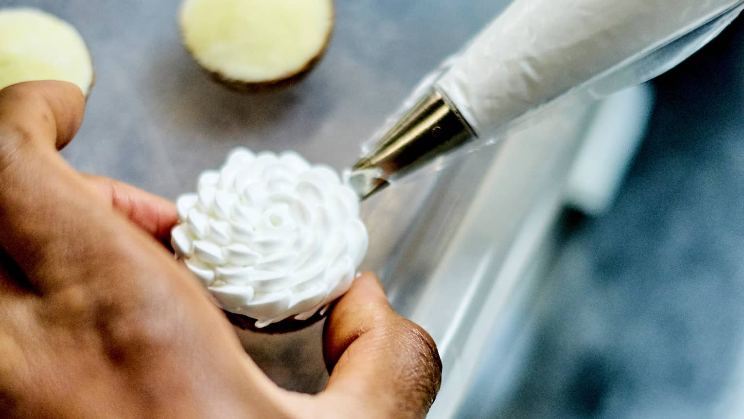 Close-up of pastry chef piping vanilla icing on cupcakes