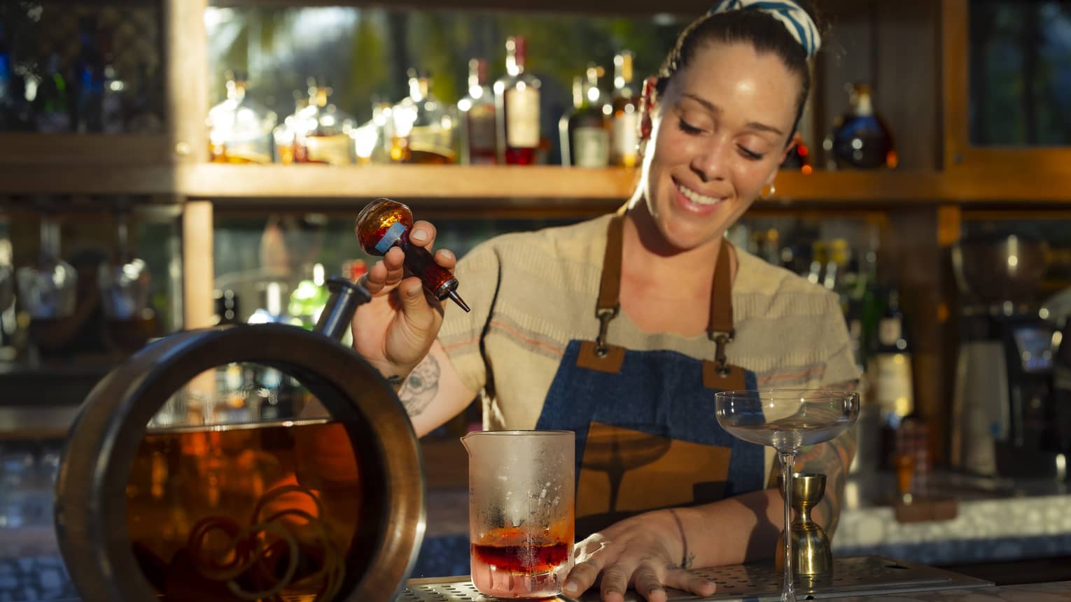 Bartender smiles as they pour an ingredient into a cocktail glass