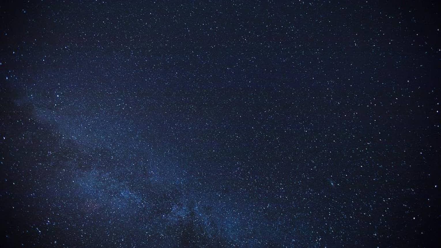 Thousands of stars dusting across a clear night sky; a cluster of stars form the Milky Way, just barely visible in the sky.