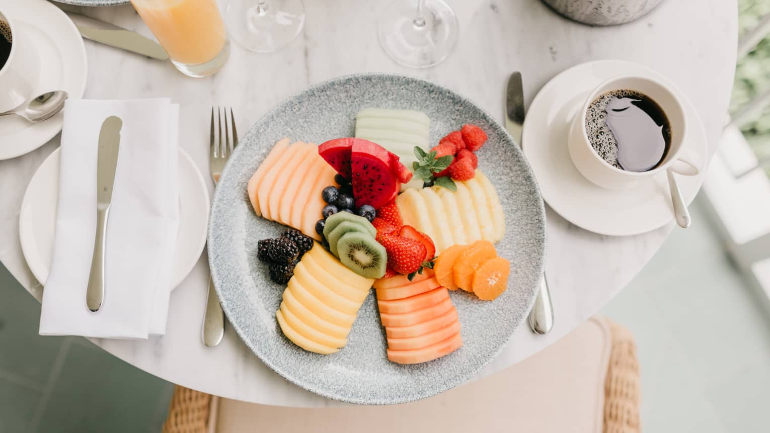 Plate of assorted sliced fruits and whole berries, place setting, coffee