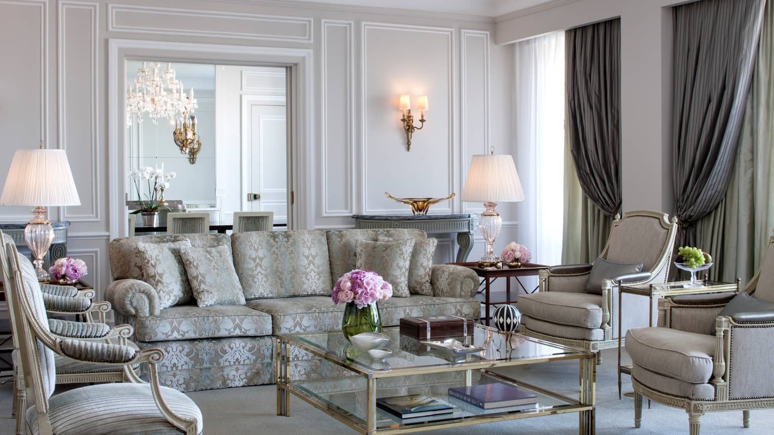 Royal Suite bright, elegant living room with blue-and-grey satin sofa, armchairs, glass coffee table with gold trim, white walls