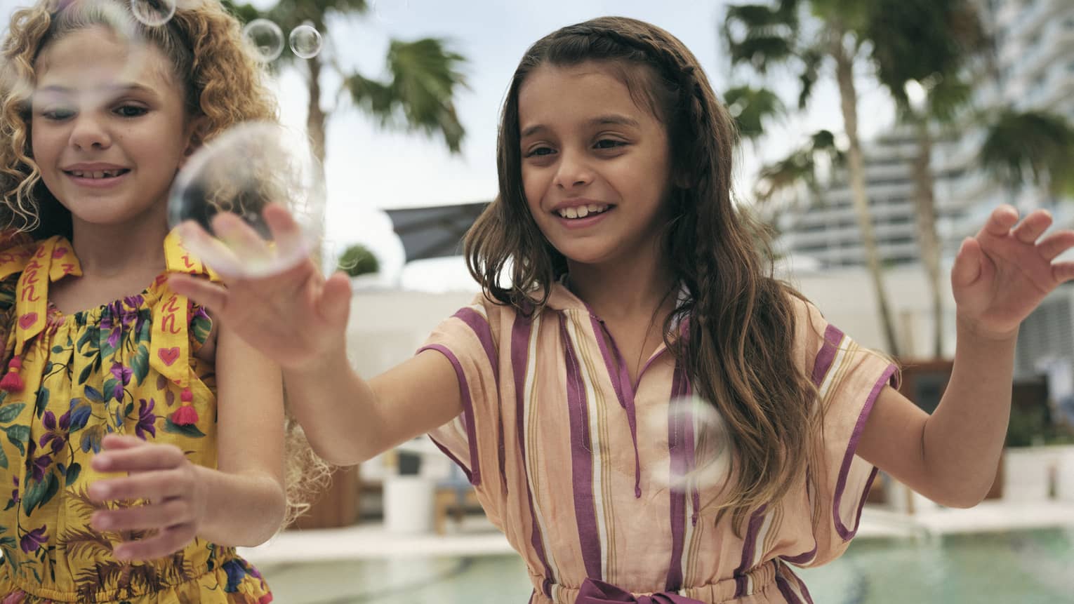 Two young girls near a pool playing with bubbles.