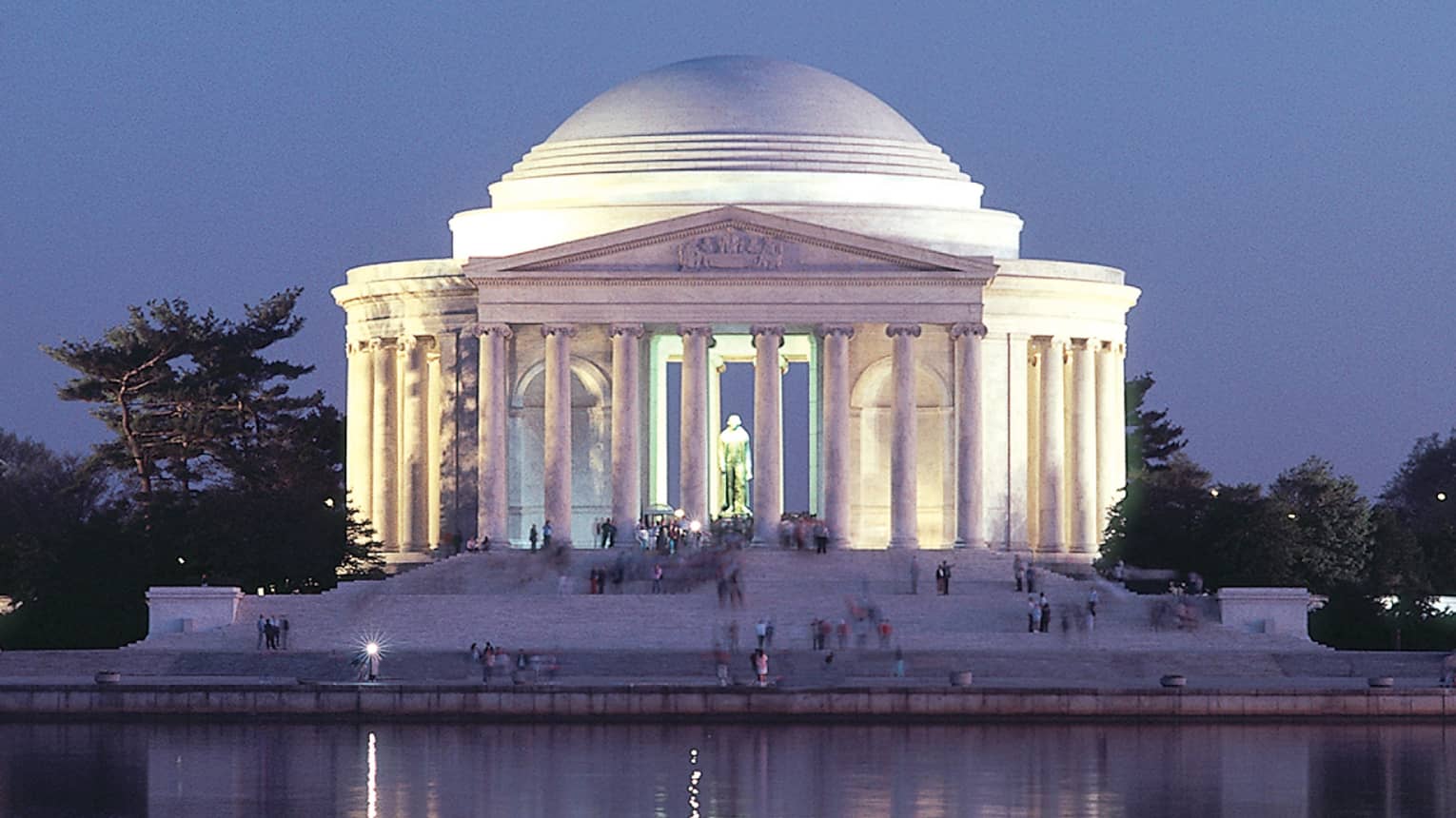 A large historical monument of white pillars and a large dome next to water.