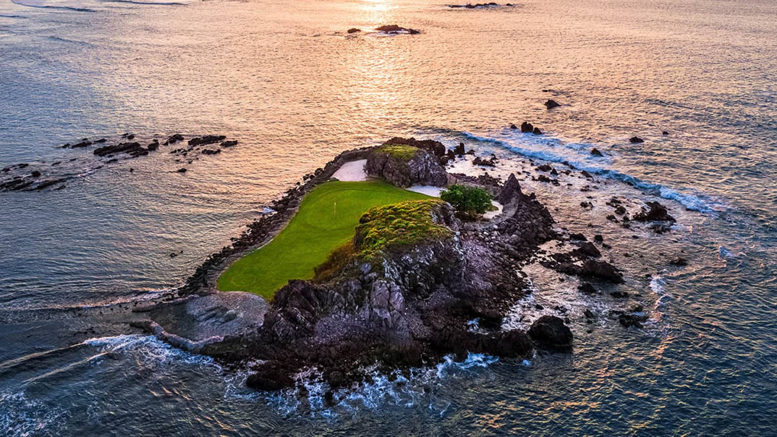 A small island that is part of a gold course, the sun is rising in the distance.