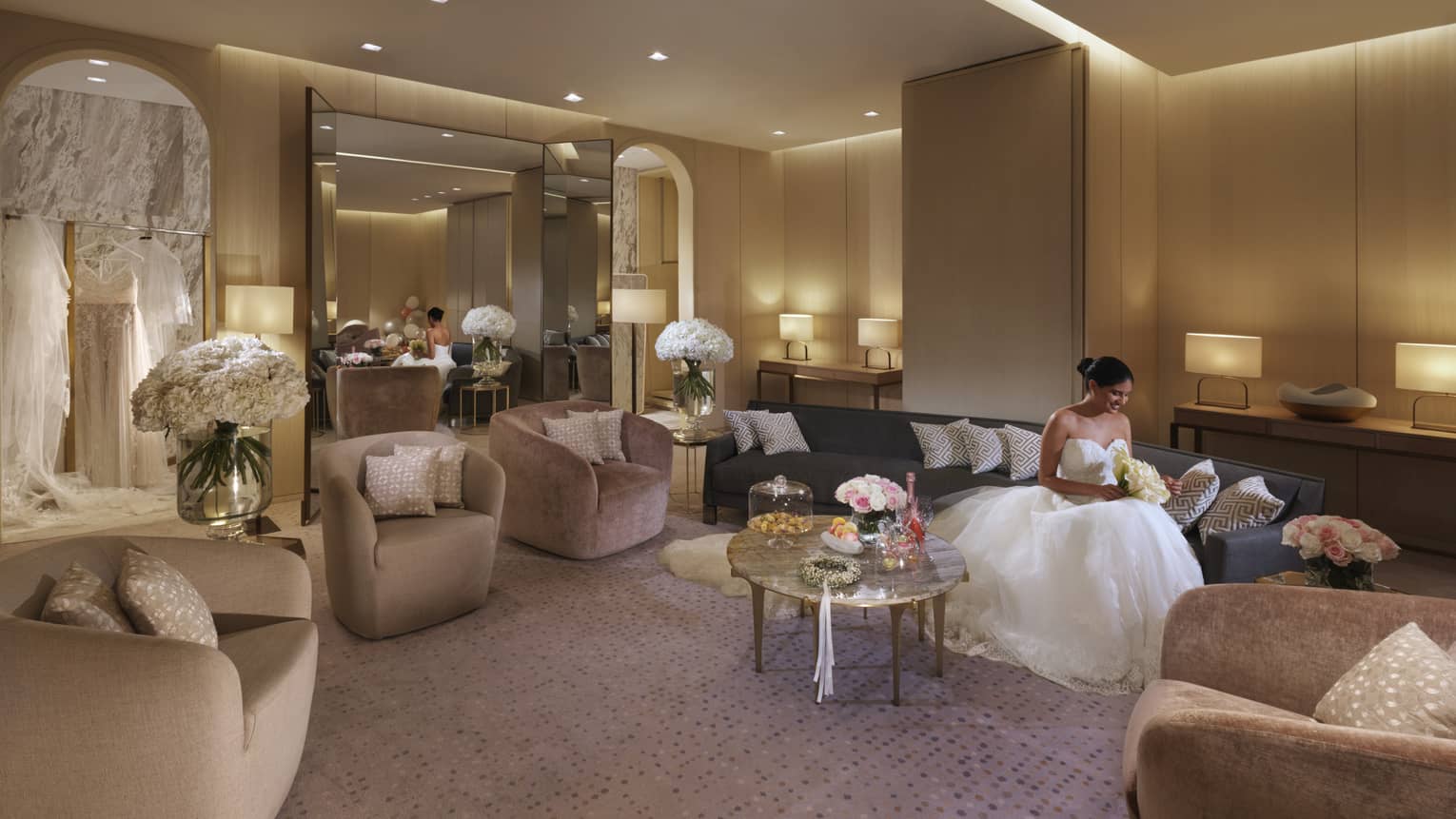 A bride dressed in her wedding dress, sits on a dark couch and reads a note in the bridal suite