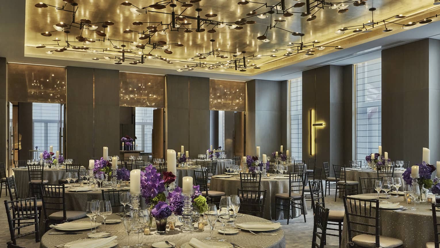 Round banquet dining tables with purple flower arrangements under modern ceiling, lights 