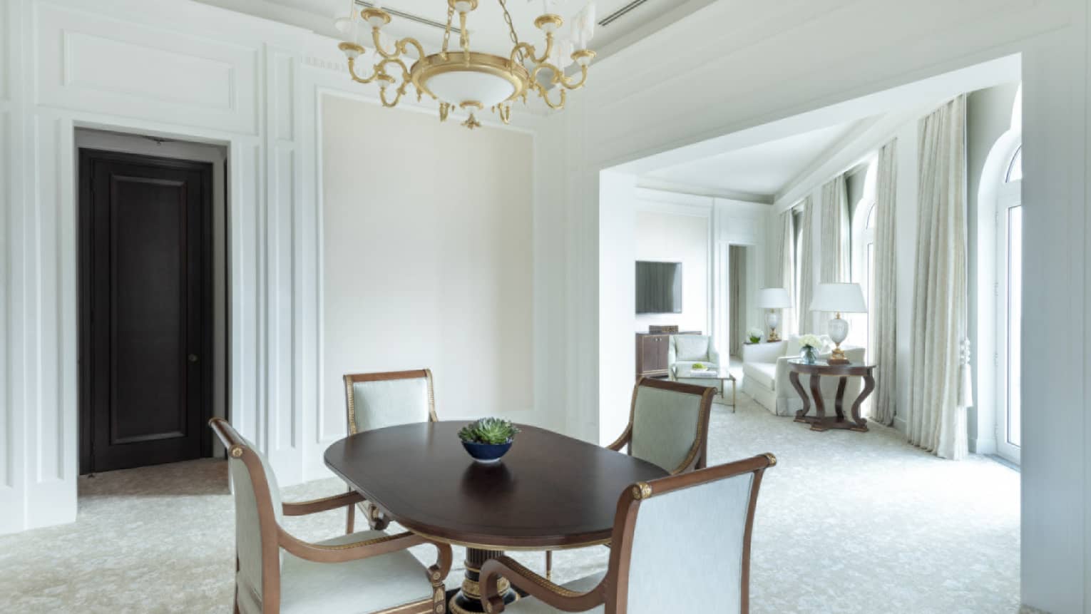Dining room with white walls, dark wooden dining table and four ivory upholstered chairs, chandelier