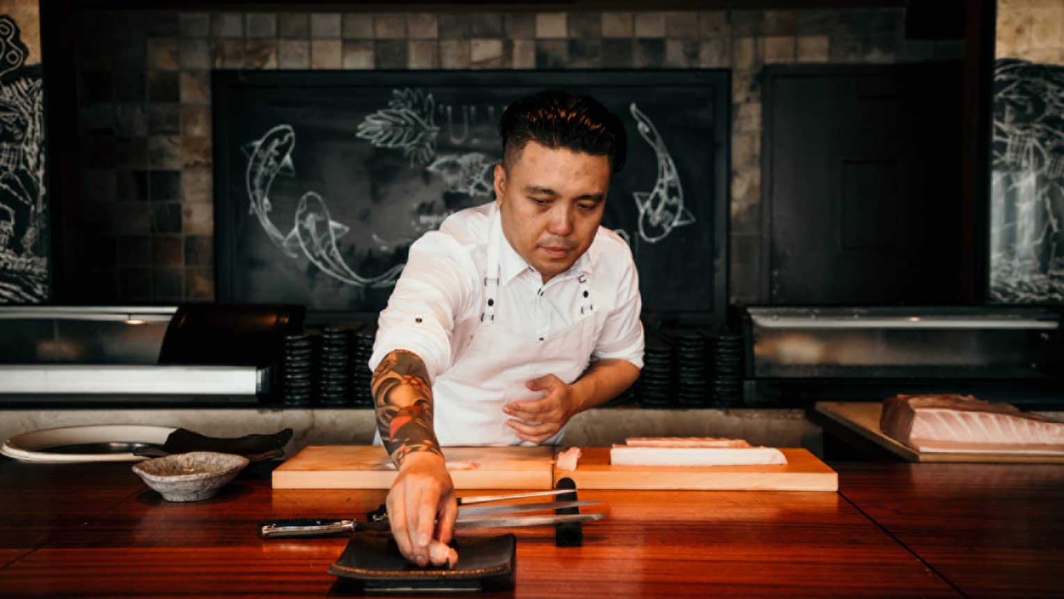 A male chef behind wooden counter places a piece of seafood on plate