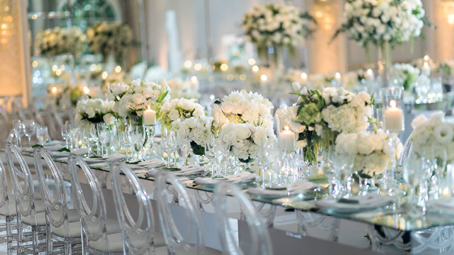Long wedding dining table filled with white flowers, lined with transparent chairs