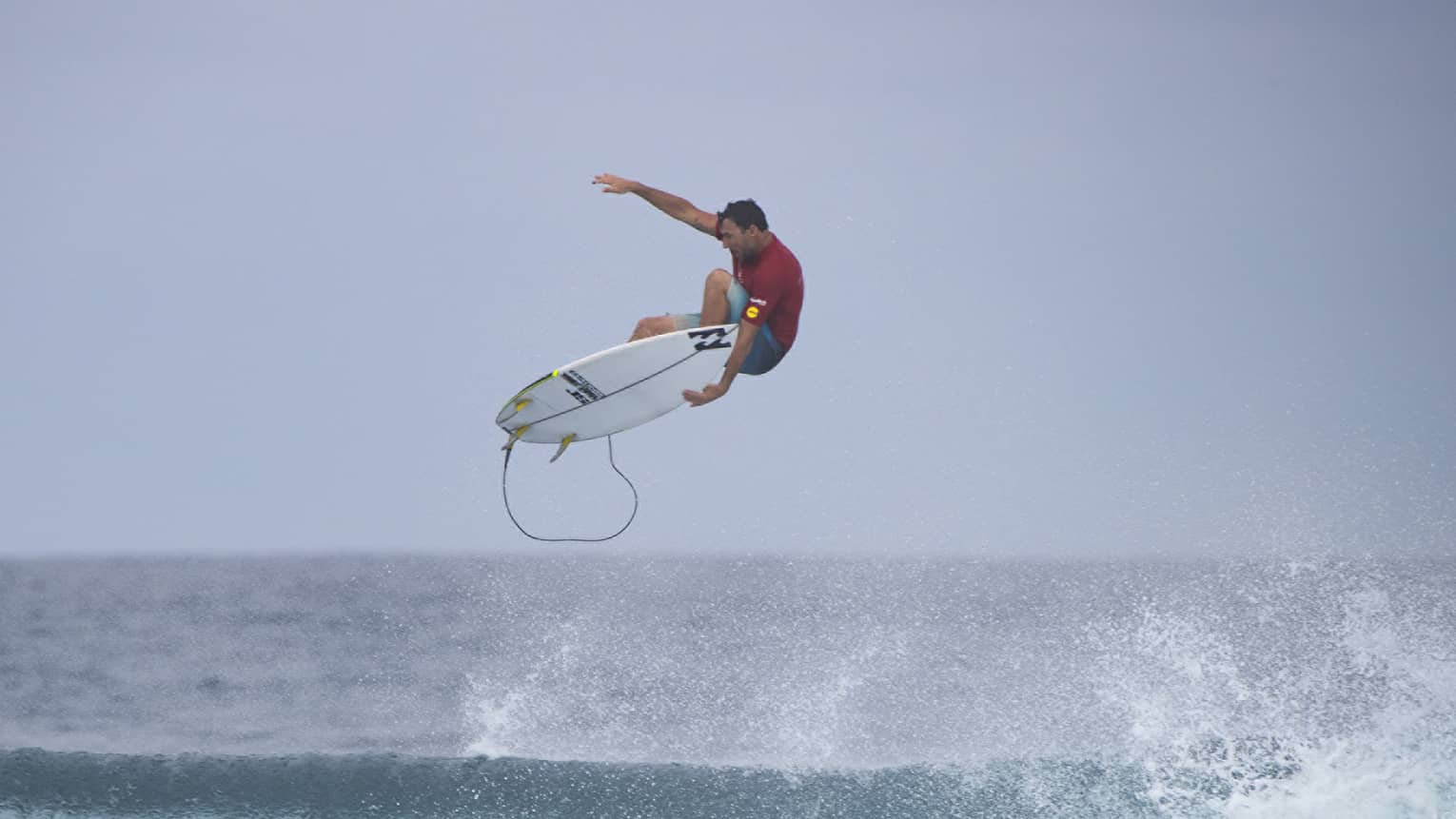 Surfer grips surfboard mid-air while riding the waves