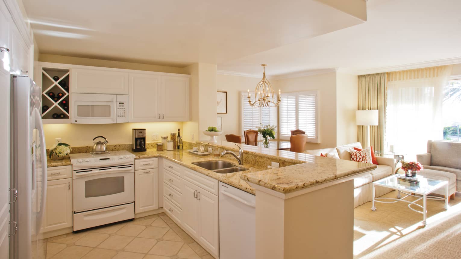 Villa kitchen with stove, dishwasher, cupboards under L-shaped marble counter, overlooking living room