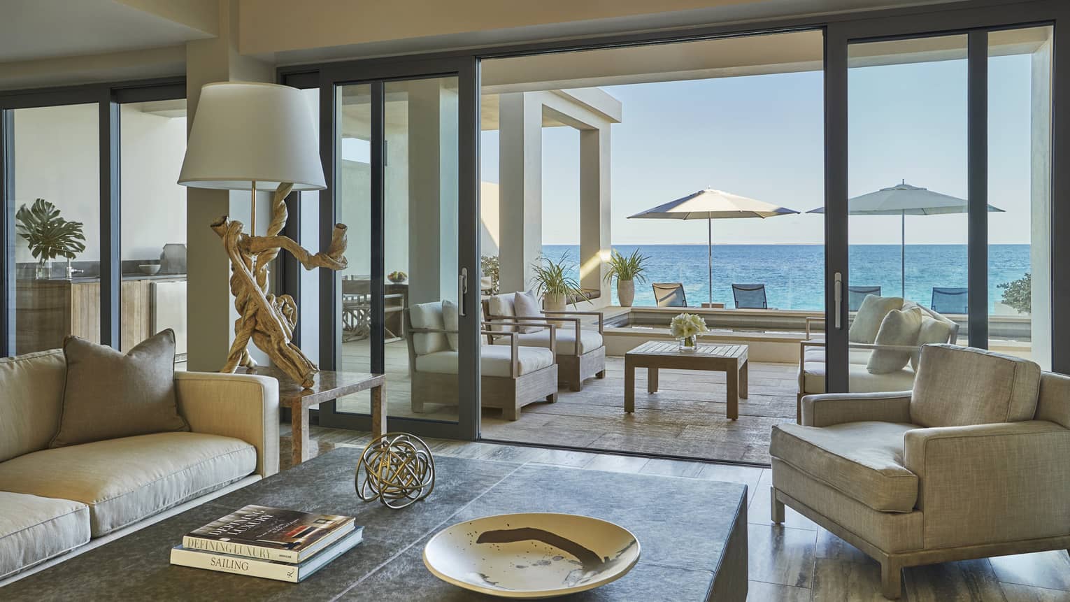 View from inside to indoor-outdoor living rooms with sofas, chairs, patio umbrellas and ocean in background