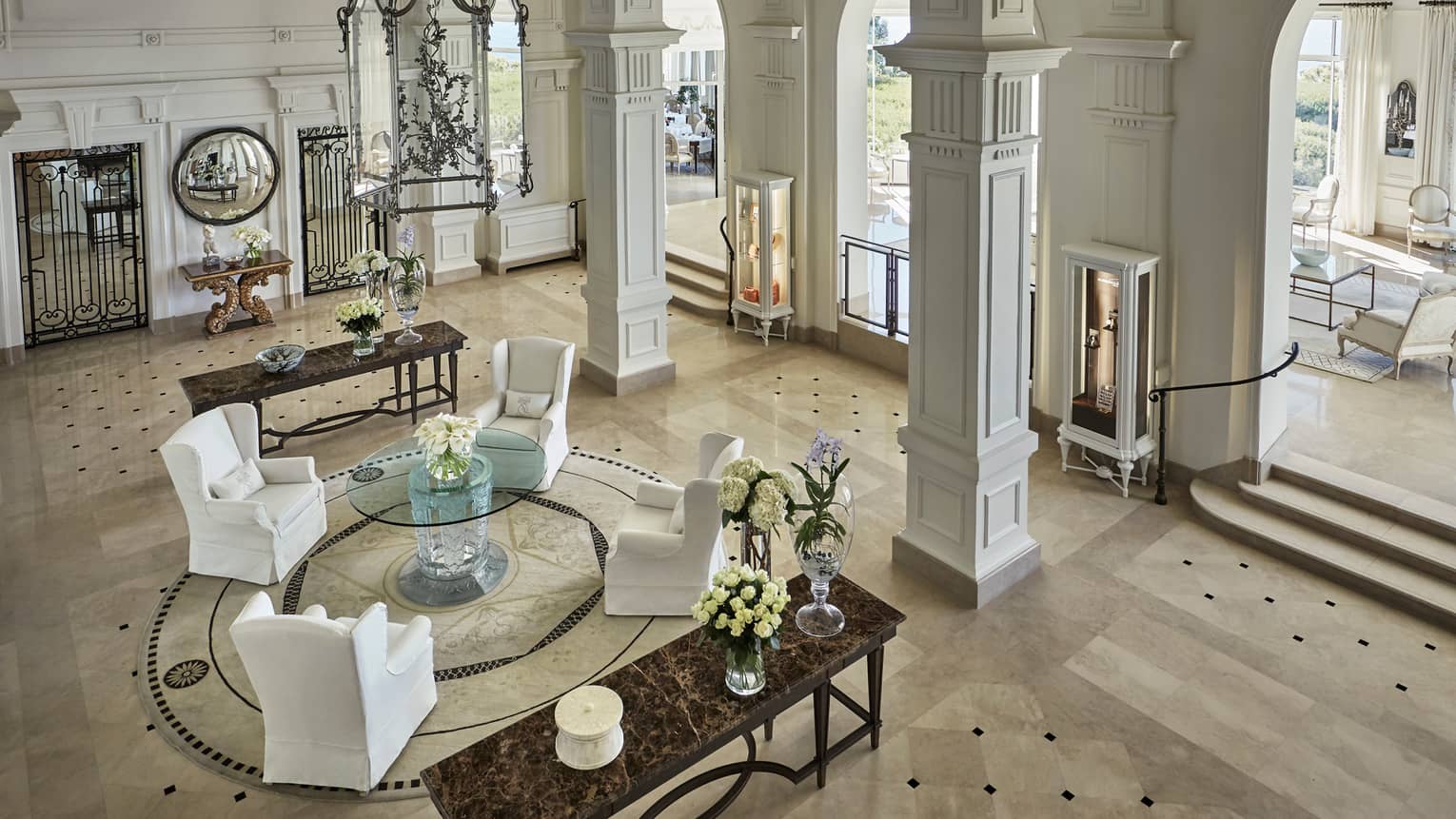 View of bright, palatial hotel lobby, white armchairs on marble floors under pillars