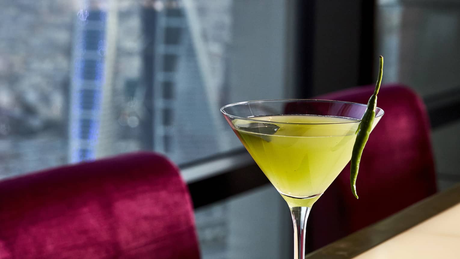 A yellow martini with a sprig of mint balanced on the lip of the glass. 