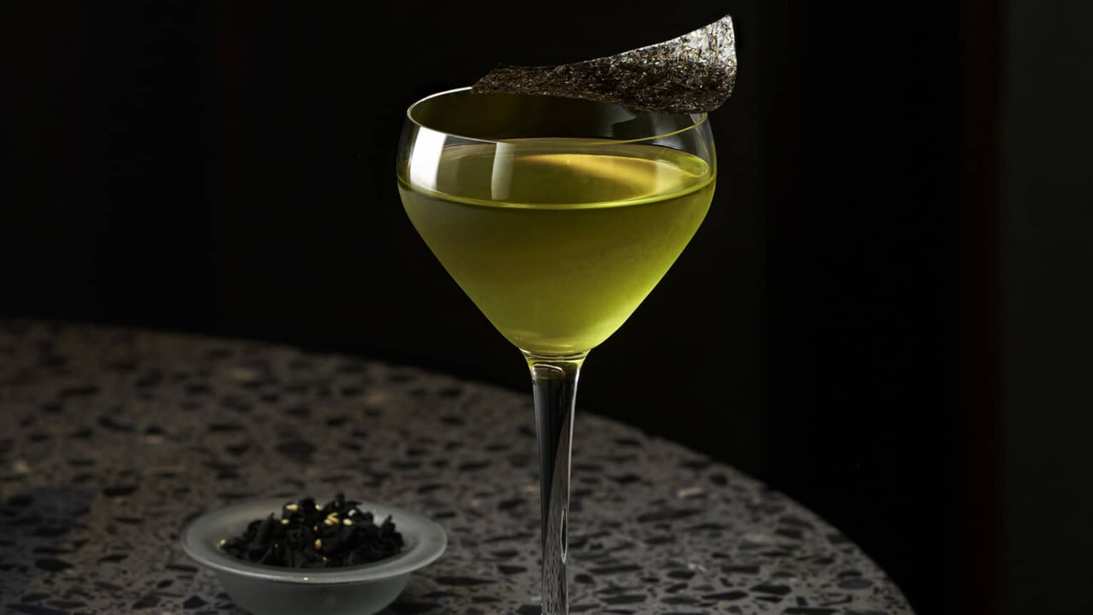Yellow-hued cocktail in stemmed glass on round grey marble table