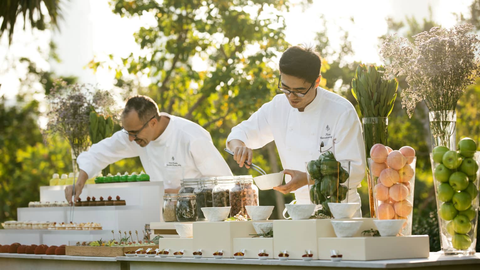 Two chefs arrange desserts on outdoor buffet