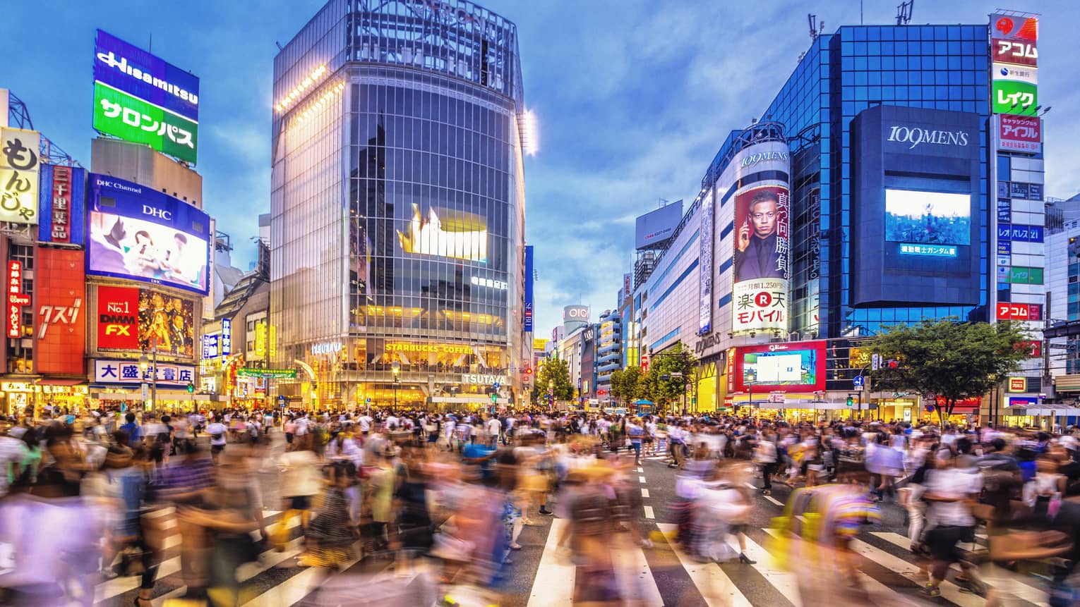 Image of blurry crowds along sidewalk under glass buildings, colourful billboards at night